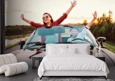 Traveling by car - happy couple in love go by cabriolet car in sunset time Wall mural