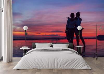 Two girlfriends hugging up and enjoying a rose/pink sunset sky on the sea beach on the Samui Island,Thailand. Calm warm countries vacation concept image. Wall mural