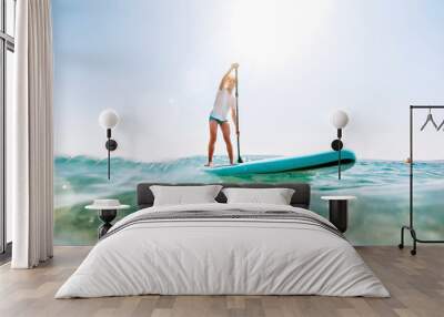 Under the water view angle to the smiling blonde teenager boy rowing stand up paddle board. Active family summer vacation time near the sea concept image. Wall mural