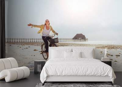 Young female dressed light summer clothes joyfully threw up her hand riding old vintage bicycle with front basket on the low tide ocean white sand coast on Kiwengwa beach on Zanzibar island, Tanzania. Wall mural