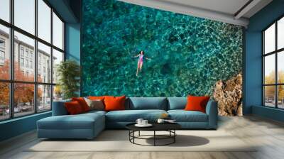 Young female floating on the back and relaxing on the warm turquoise Adriatic sea waves with rocky coastline. Carefree people vacation time concept aerial top view image. Wall mural