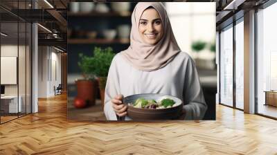 Arab woman standing in modern kitchen holding salad bowl and smile for the camera Wall mural