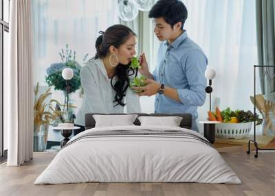 Portrait of happy young couple cooking together in the kitchen at home. Loving couple preparing vegetable salad for dinner Wall mural