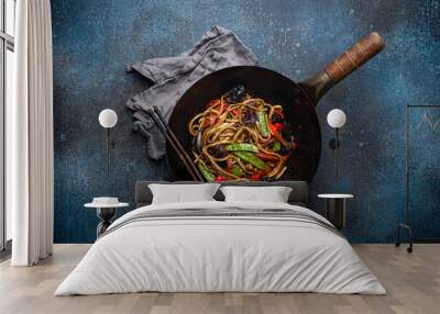 Asian dish stir fry udon noodles with vegetables and mushrooms in black rustic wok pan with wooden chopsticks on rustic dark blue concrete background from above, Chinese fast food Wall mural