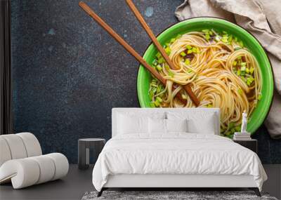 Asian noodles soup in green rustic ceramic bowl with wooden chopsticks top view on rustic stone background. Lo mein noodles with bouillon and green onion, space for text Wall mural