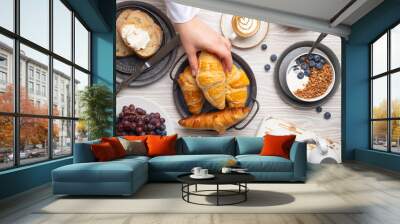 Beautiful morning breakfast gathering with fresh croissants, granola with yoghurt and berries, toasts, coffee cappuccino and fruit on plate. Tasty and healthy breakfast, white wooden table, top view . Wall mural