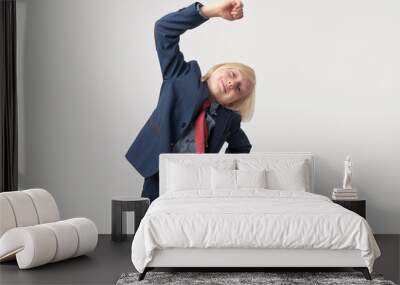 Cute little boy in blue suit and red tie doing exercises against white background Wall mural