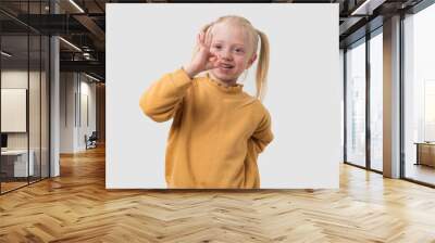 Cute little girl with blond hair, dressed in a yellow sweater, showing OK sign with both hands, isolated on white background Wall mural