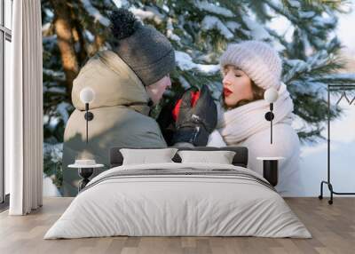 Loving couple in winter forest. Young man warms the hands of his beloved with his breath. Dating in park Wall mural