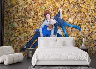 Mother and two children lies on yellow leaves in Park. Family having fun in forest. Top view. Wall mural