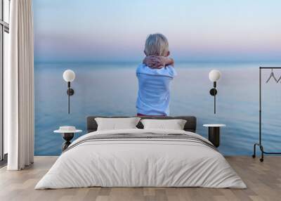 Rear view of child in sunset and sea background. Children's loneliness concept Wall mural