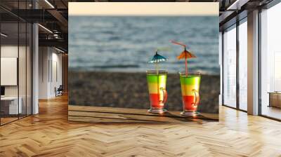 Two cocktails with straws on a wooden table top in the sun on the beach, empty space Wall mural