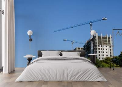 two construction cranes against a background of blue sky and green trees. a horizontal view Wall mural