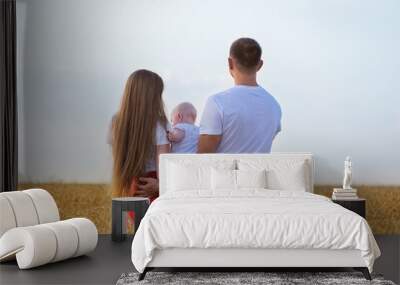 Young family in wheat field with small child. Mom dad and baby. Back view. Wall mural