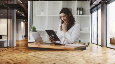 Businesswoman using tablet and laptop computer working at desk in office. Wall mural