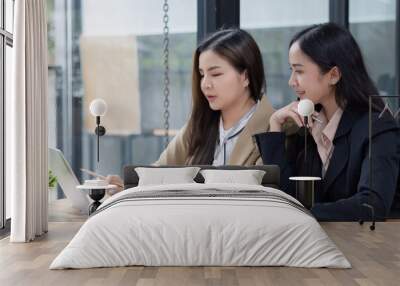 Two Asian businesswomen working on laptop computer with analyzing financial charts in the modern office, Business financial documents and planning idea project concept. Wall mural