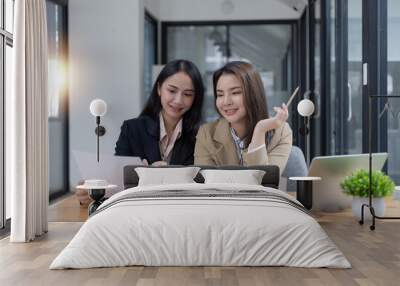 Two Asian businesswomen working on laptop computer with analyzing financial charts in the modern office, Business financial documents and planning idea project concept. Wall mural