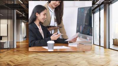 Two Asian young businesswomen working on computer with analyzing financial charts in the modern office, Business financial documents and planning idea project concept. Wall mural