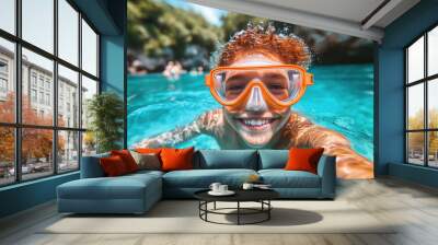 A cheerful boy wearing orange goggles swims in turquoise water, surrounded by greenery and enjoying a sunny afternoon in a natural setting Wall mural