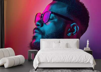 A man in glasses confidently poses against vibrant hues of blue, pink, and purple lighting Wall mural