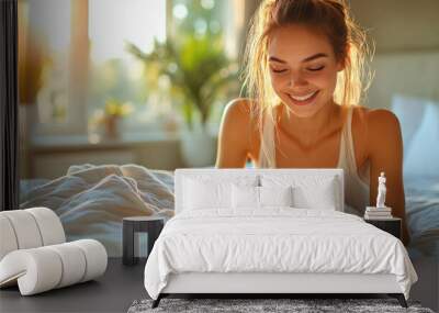 A woman smiles warmly as she relaxes on her bed, soaking in the morning sunlight streaming through the window Wall mural