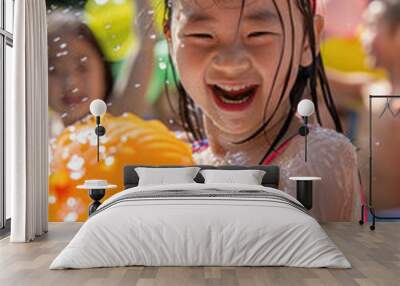 A young girl smiles brightly as she holds a water balloon in her hand, surrounded by a spray of water Wall mural