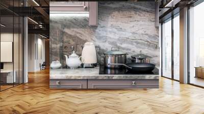 cream electric kettle with porcelain tea accessories on granite countertop next to ceramic hob with steel pots and pan Wall mural