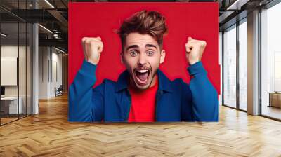 Portrait of handsome man who received amazing news, looking at camera, raising arm in winners gesture and screaming yeah on red background, created with Generative AI Wall mural