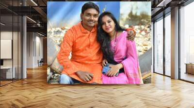 Married indian couple sitting together wearing traditional ethnic dress looking at each other happily. Wedding day in the park outdoor in the background, city Wall mural