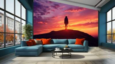 Silhouette of a person standing on a hill against a vibrant sunset, with dramatic colors and a serene atmosphere, emphasizing solitude and reflection. Wall mural