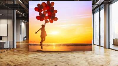 happiness or dream concept, silhouette of happy woman jumping with multicolored balloons at sunset on the beach Wall mural