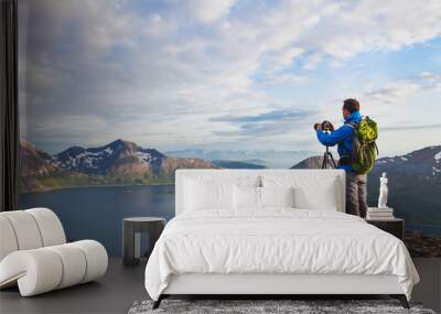 landscape photographer working with tripod and dslr camera in beautiful wild nature, standing with backpack on top of mountain Wall mural