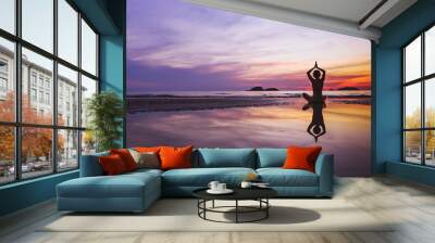 mindful meditation background, silhouette of woman doing yoga on the beach at sunset with reflection Wall mural