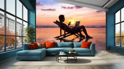 silhouette of successful business man reading emails on laptop on the beach at sunset, freelance job Wall mural