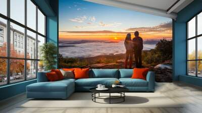 Young couple watching the sun rise from top of mountain Wall mural