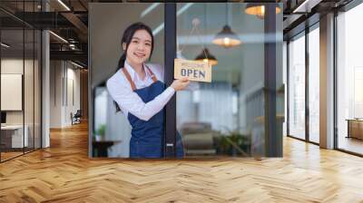 A female barista holding a coffee shop welcome sign in front of the coffee shop.  Wall mural