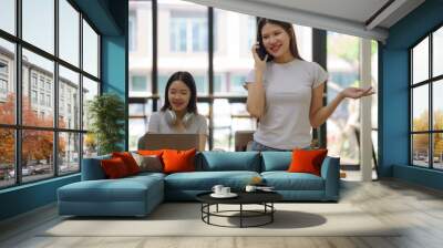 Happy young Asian businesswoman holding a mobile phone in her workstation office. Wall mural