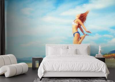 Excited young woman having fun on beach in summer. Side view of carefree youthful female tourist enjoying freedom and jumping on sandy seashore Wall mural