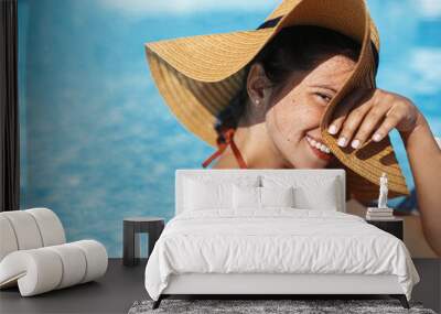 Beautiful happy carefree woman in hat relaxing in pool, enjoying summer vacation. Portrait of smiling young female sunbathing and resting at swimming pool at tropical resort. Holidays and travel Wall mural