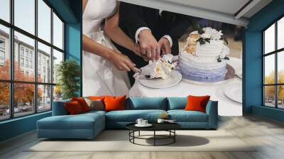 gorgeous bride and stylish groom cutting their stylish wedding cake with flower decoration at wedding reception in restaurant. happy newlywed couple emotional moment Wall mural