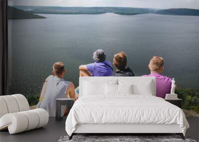 Group of hipster travelers sitting on top of rock mountain and enjoying  amazing view on river. Young friends explorers relaxing and traveling. Atmospheric tranquil moment. Copy space Wall mural