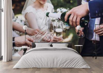 happy group of people toasting with champagne. man holding bottle of champagne and pouring drink into glasses. bride bridesmaids and groom groomsmen having fun. holiday celebration Wall mural