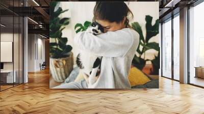 Happy hipster girl hugging cute cat, sitting together at home during coronavirus quarantine. Stay home stay safe. Isolation at home to prevent virus epidemic. Young woman with cat in modern room Wall mural