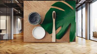 Natural toothpaste activated charcoal and bamboo toothbrush on wooden background with green monstera leaf. Plastic free beauty essentials, teeth care. Zero waste concept. Sustainable lifestyle. Wall mural