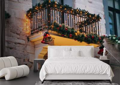 Stylish christmas decorations, red jingle bells, lights, fir branches with ornaments  on balcony  in european city street. Festive decor and illumination in city center, winter holidays Wall mural