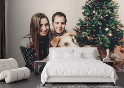 stylish hipster couple in sweaters playing with dog and smiling at christmas tree in festive room. atmospheric moments. merry christmas and happy new year concept. happy holidays Wall mural