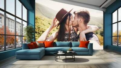 stylish hipster couple taking selfie and kissing on top of mountains in sunny summer day. beautiful man and happy woman in hat embracing on honeymoon. travel together Wall mural