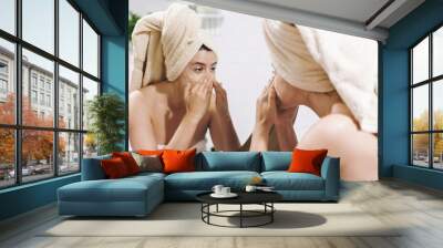 Young happy woman in towel applying organic face mask and looking at round mirror in stylish bathroom. Girl making facial massage with scrub, peeling and cleaning skin on face. Skin Care Wall mural