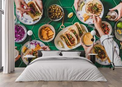 Friends home taco party. Flat-lay of Mexican traditional dishes Tacos with beef meat, corn tortillas , tomato salsa and peoples hands with food over green background, top view. Mexican cuisine Wall mural