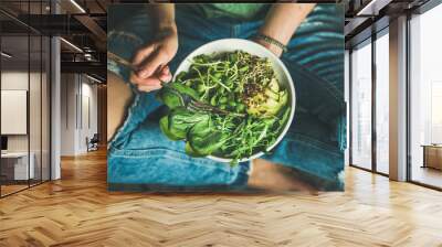 green vegan breakfast meal in bowl with spinach, arugula, avocado, seeds and sprouts. girl in jeans  Wall mural